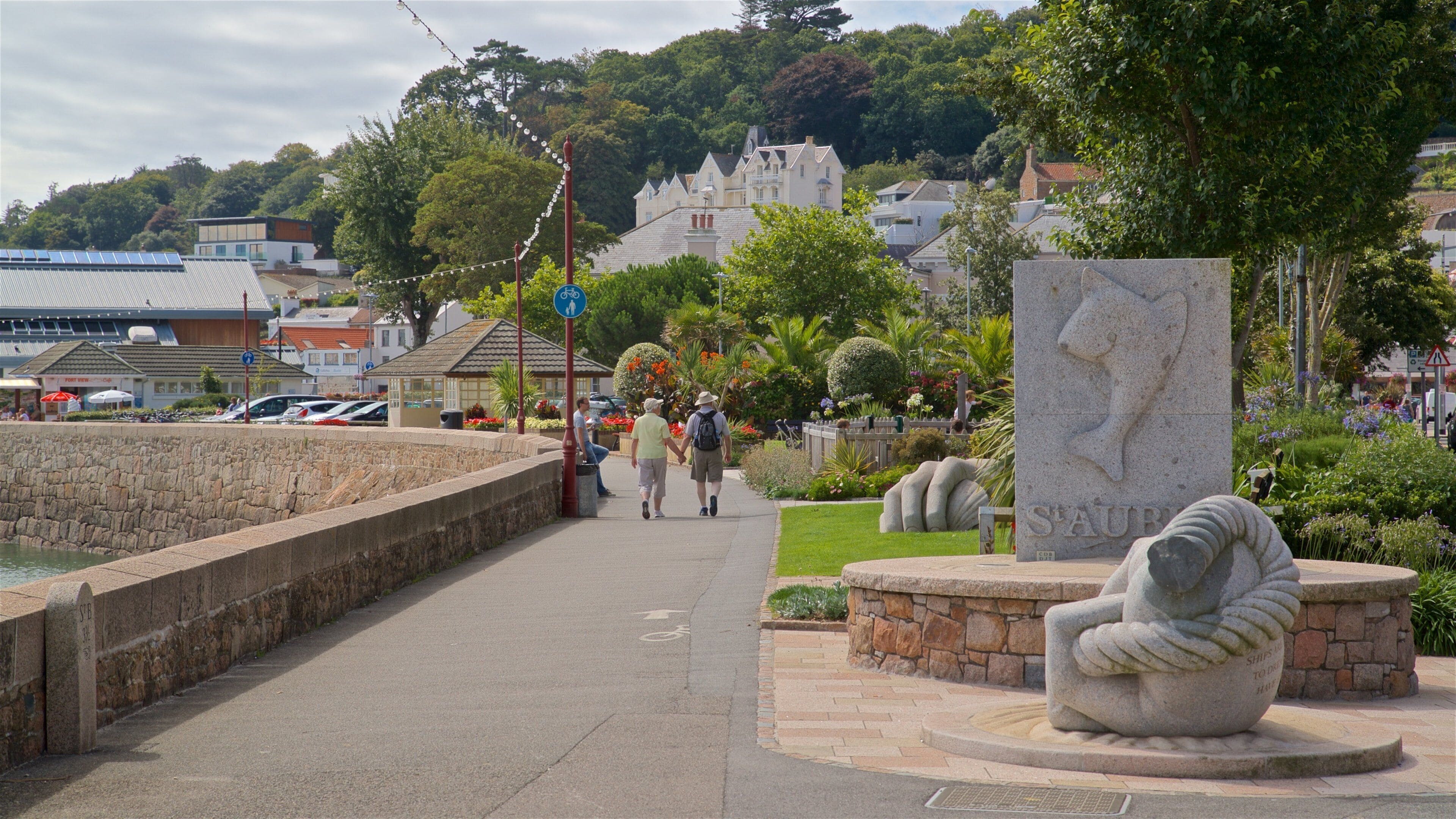 A stone wall, a statue, and a pathway with people walking.
