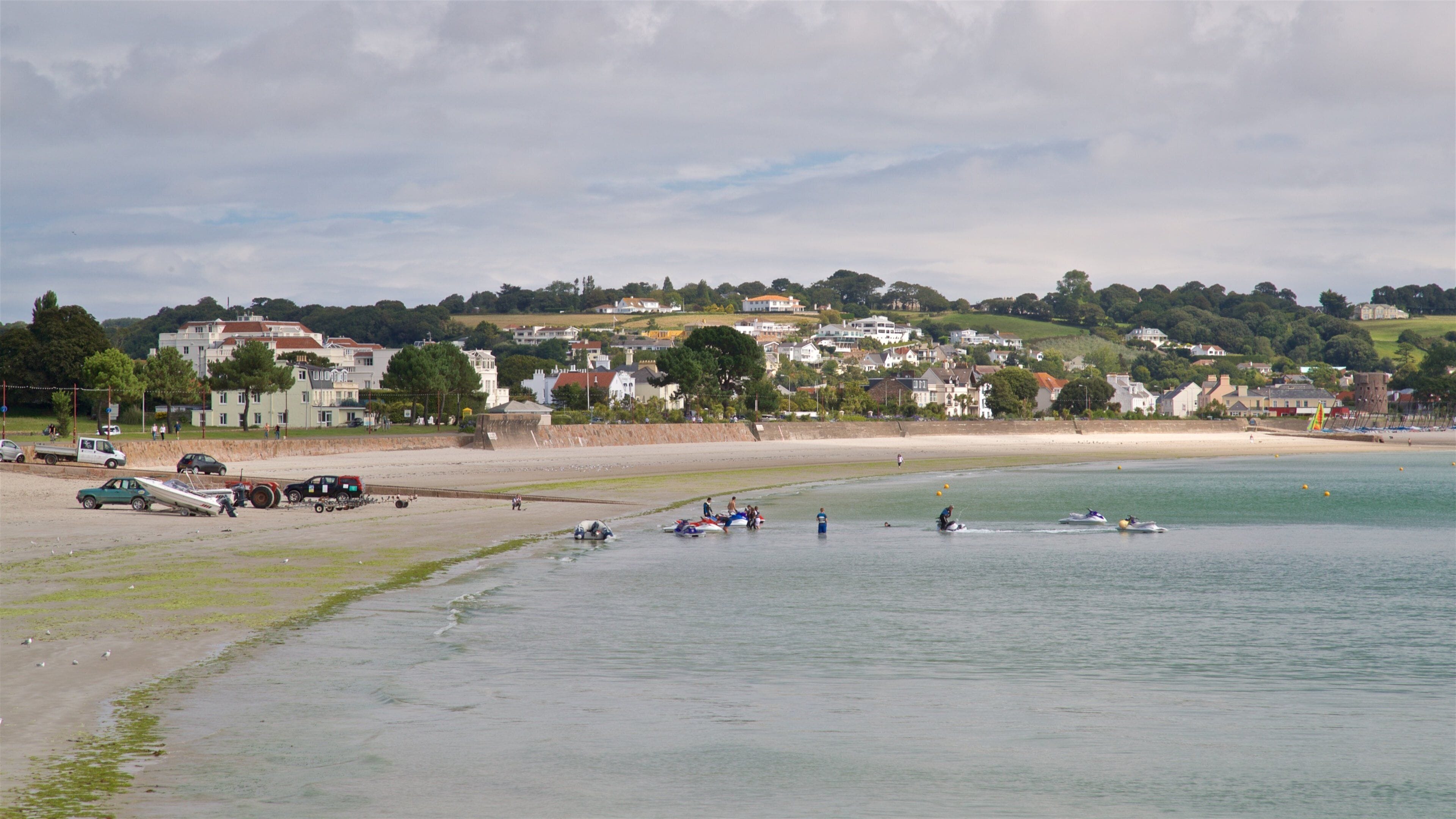 A coastal town with a sandy beach, calm water, and houses in the background.