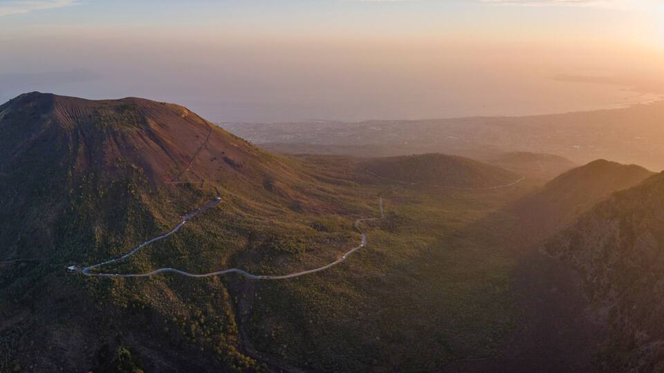 A winding road through a mountainous landscape with a sunset in the background.