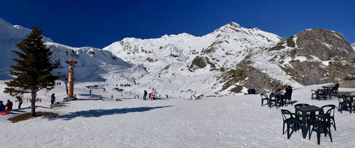 A snowy mountain landscape with a ski lift, a wooden totem, and outdoor seating.