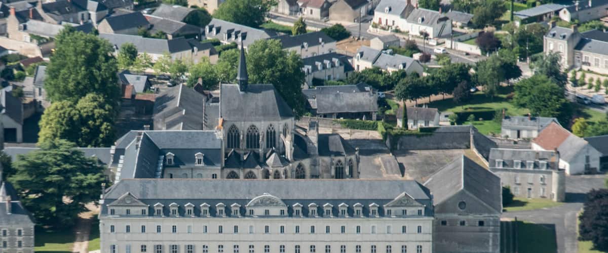 An aerial view of a historic building with a symmetrical garden and surrounding residential area.