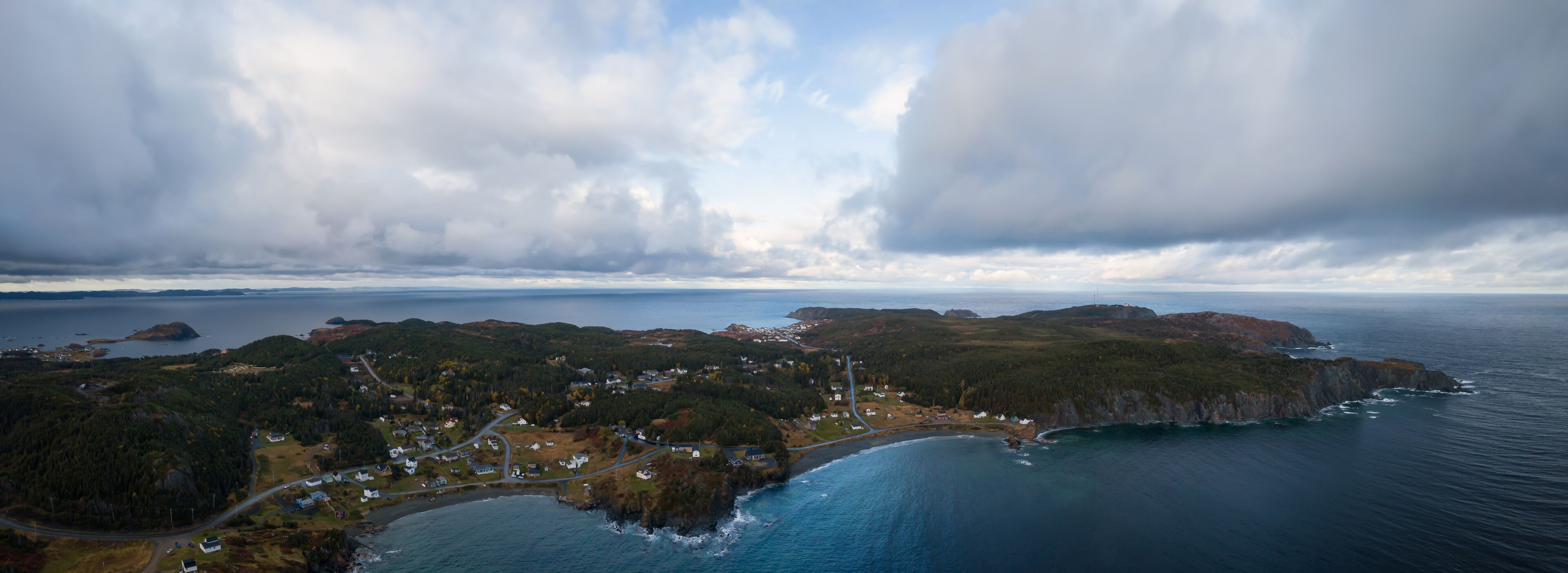 An aerial view of a coastal town with houses, roads, and a lighthouse.