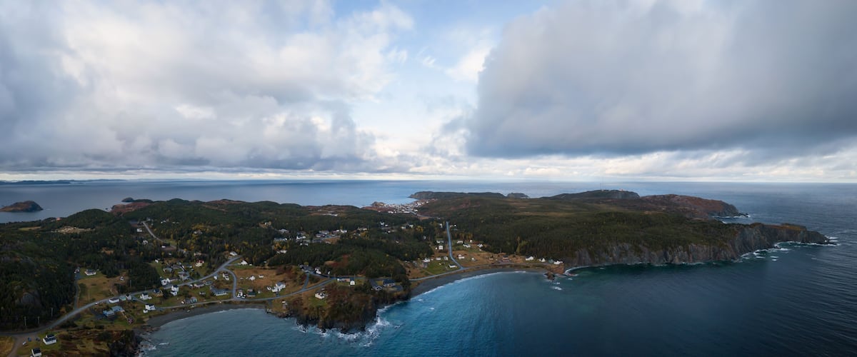 An aerial view of a coastal town with houses, roads, and a lighthouse.