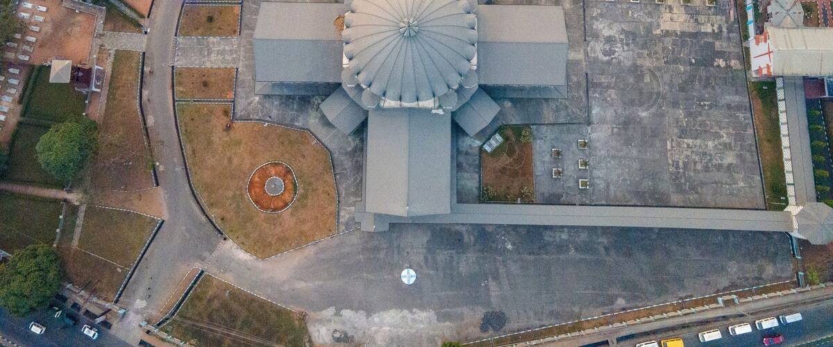 An aerial view of a large, circular building with a central dome, surrounded by a paved area and smaller structures.