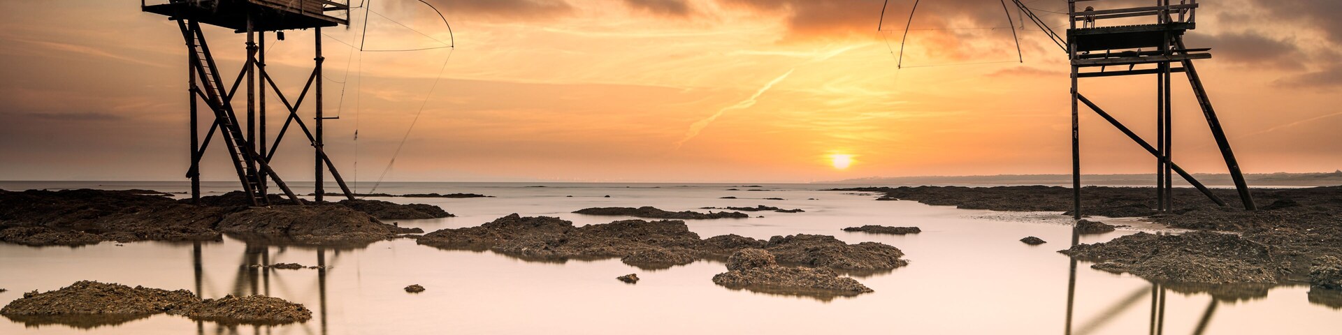 Un atardecer sobre una playa tranquila con dos estructuras de madera sobre pilotes.