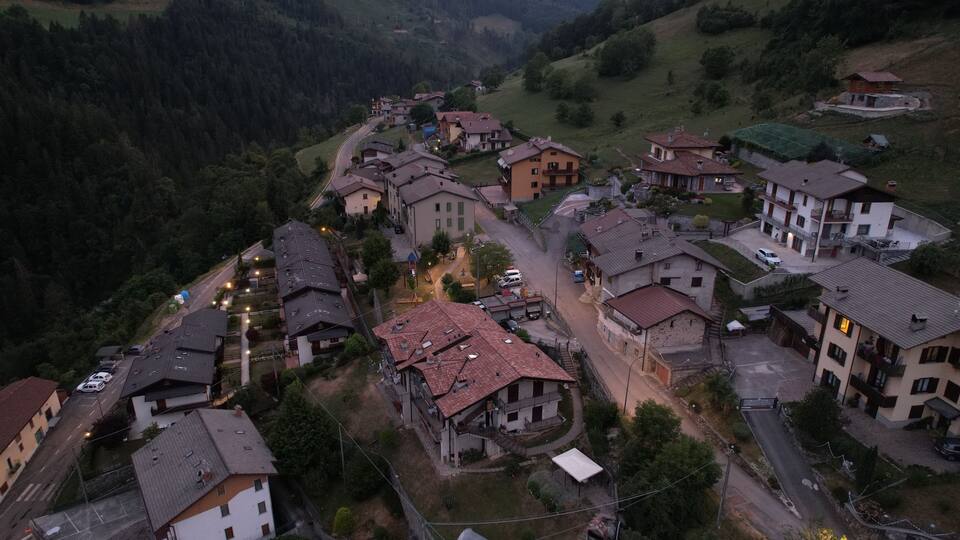 A village with houses and a winding road surrounded by greenery and hills.