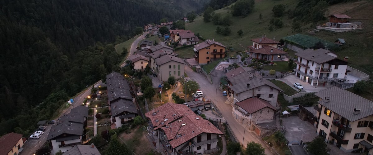 A village with houses and a winding road surrounded by greenery and hills.