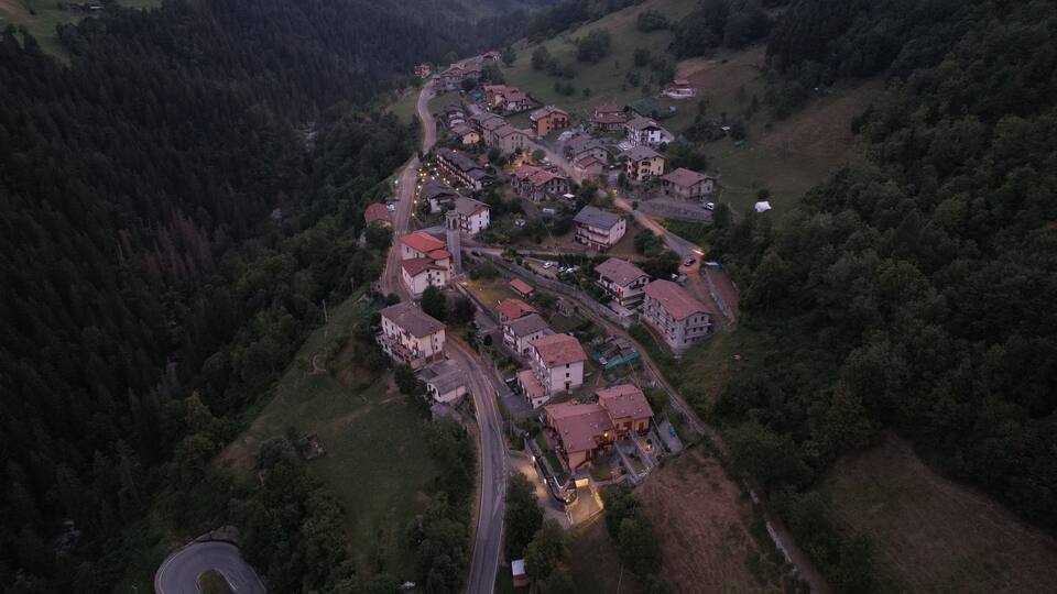 An aerial view of a village with houses, roads, and surrounding forest.