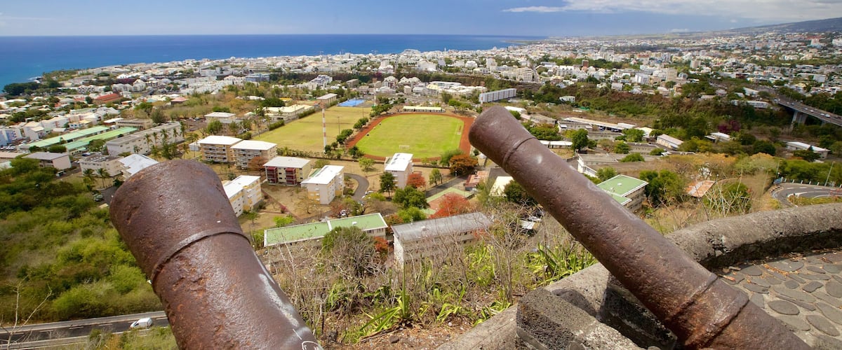 A coastal cityscape with a large green sports field, residential buildings, and a view of the ocean.