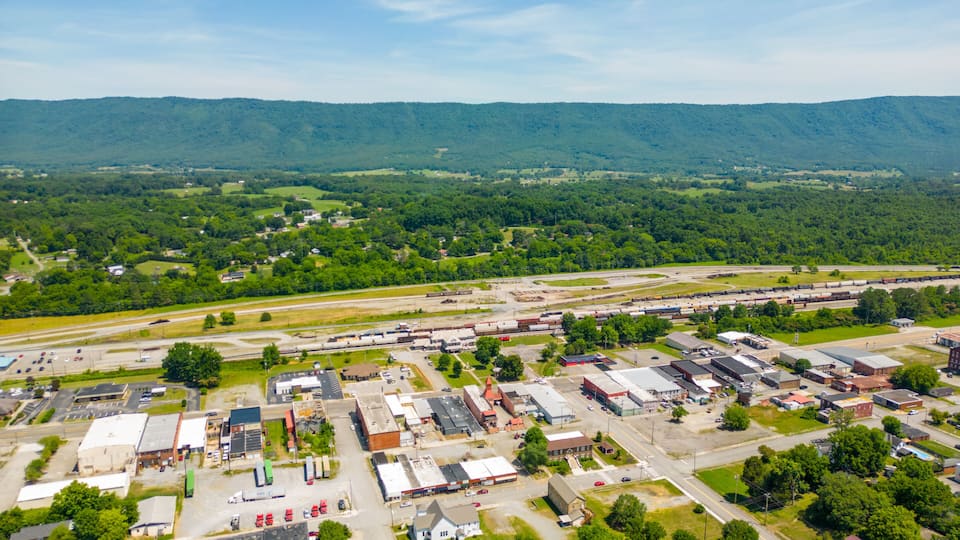 An aerial view of a small town with a train yard, surrounded by green hills.
