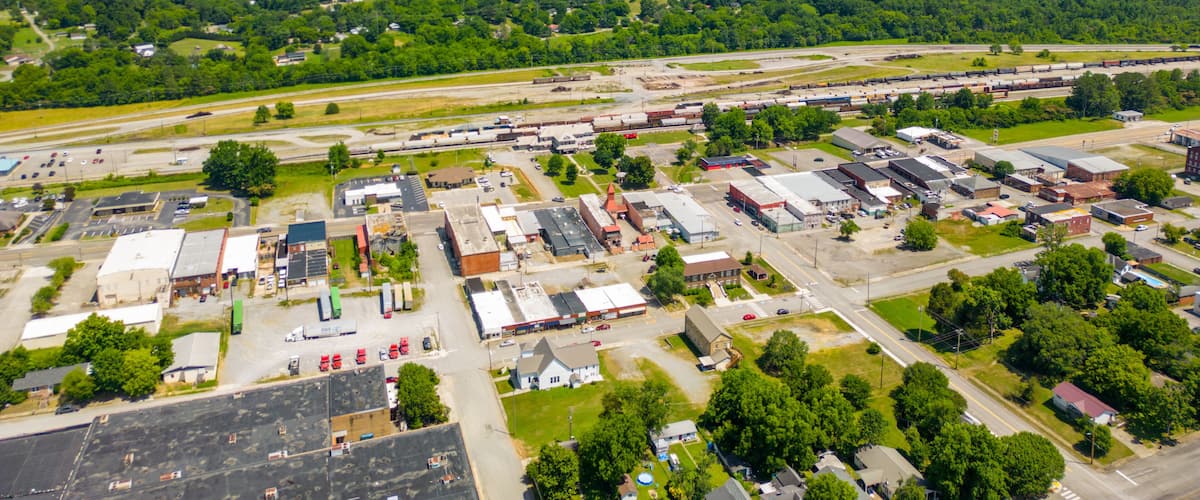 An aerial view of a small town with a train yard, surrounded by green hills.