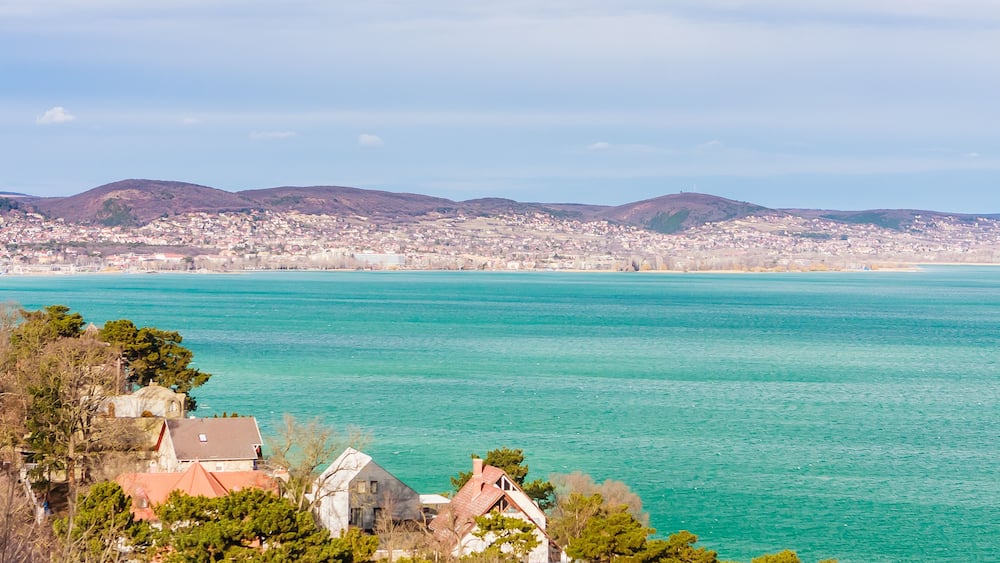 A coastal town with turquoise waters, a church, and rolling hills in the background.