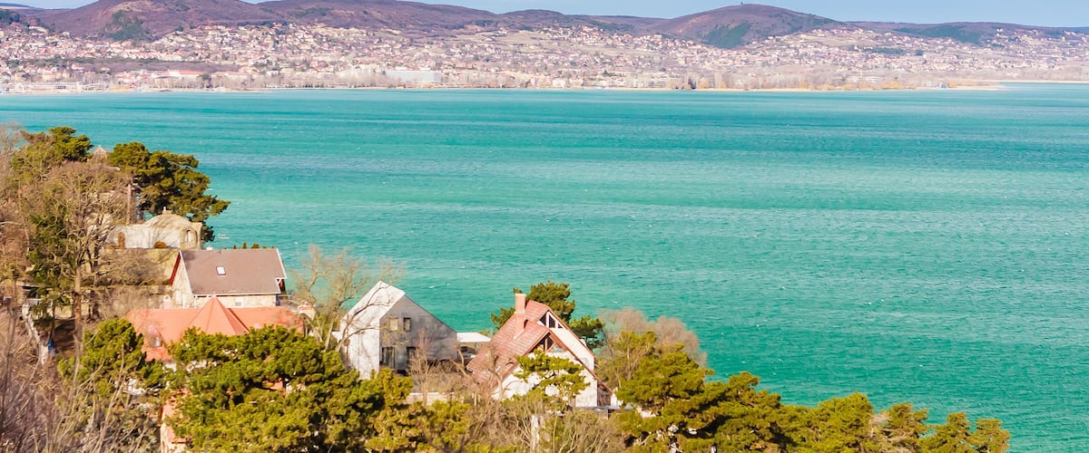 Une ville côtière aux eaux turquoise, avec une église et des collines verdoyantes en arrière-plan.