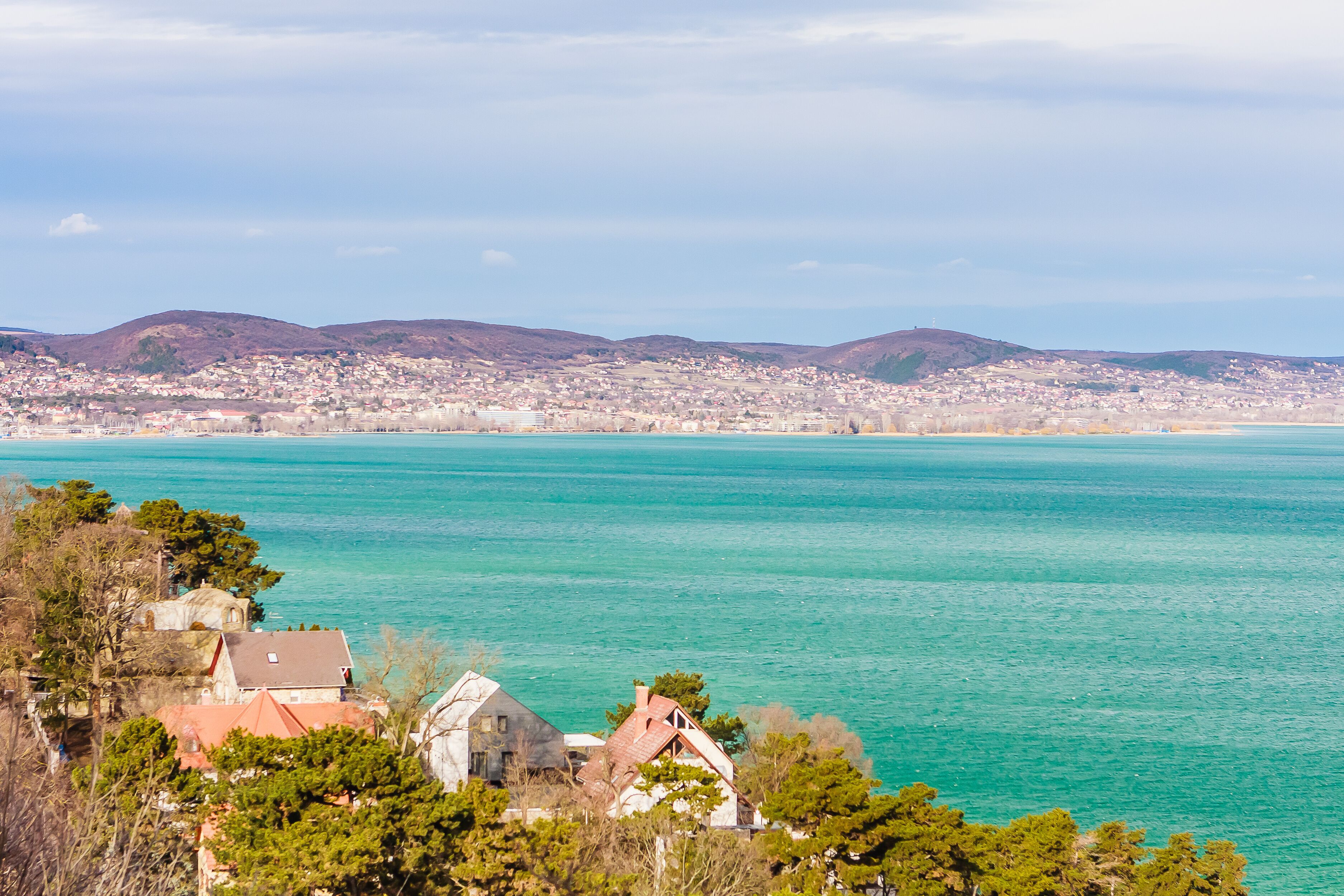 A coastal town with turquoise waters, a church, and rolling hills in the background.
