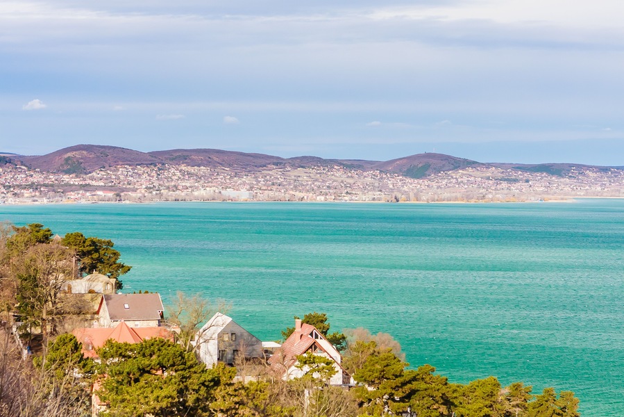 Une ville côtière aux eaux turquoise, avec une église et des collines verdoyantes en arrière-plan.