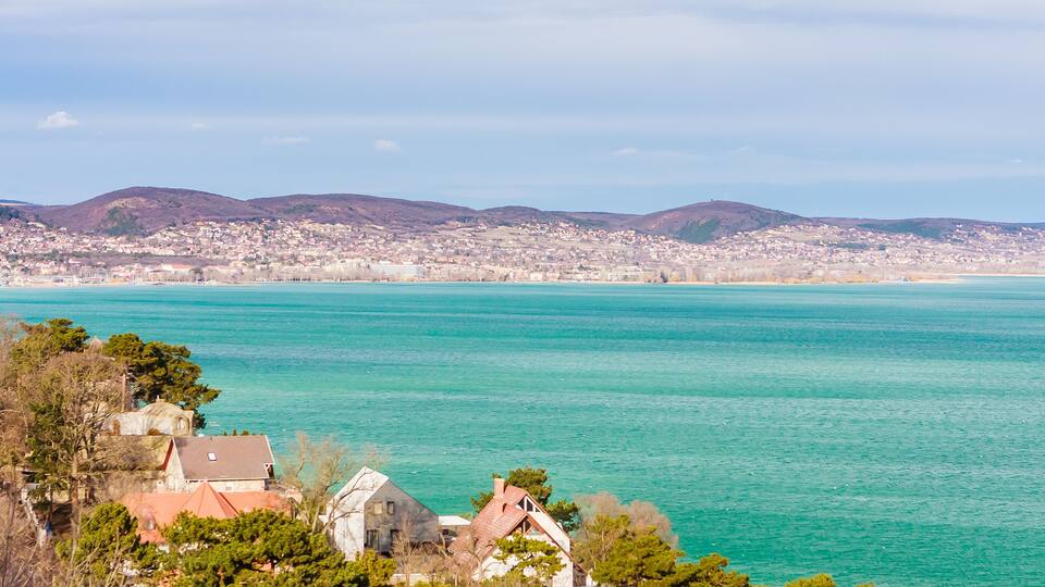 A coastal town with turquoise waters, a church, and rolling hills in the background.