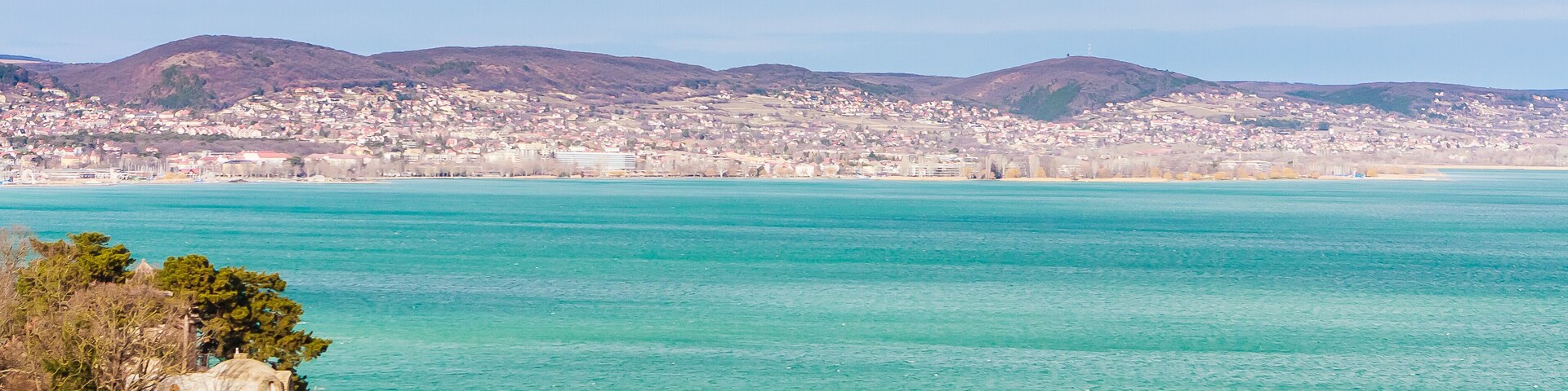 Uma cidade costeira com águas azul-turquesa, uma igreja e colinas suaves ao fundo.