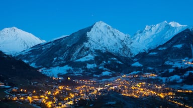 A snow-covered mountain range at dusk with a town illuminated below.