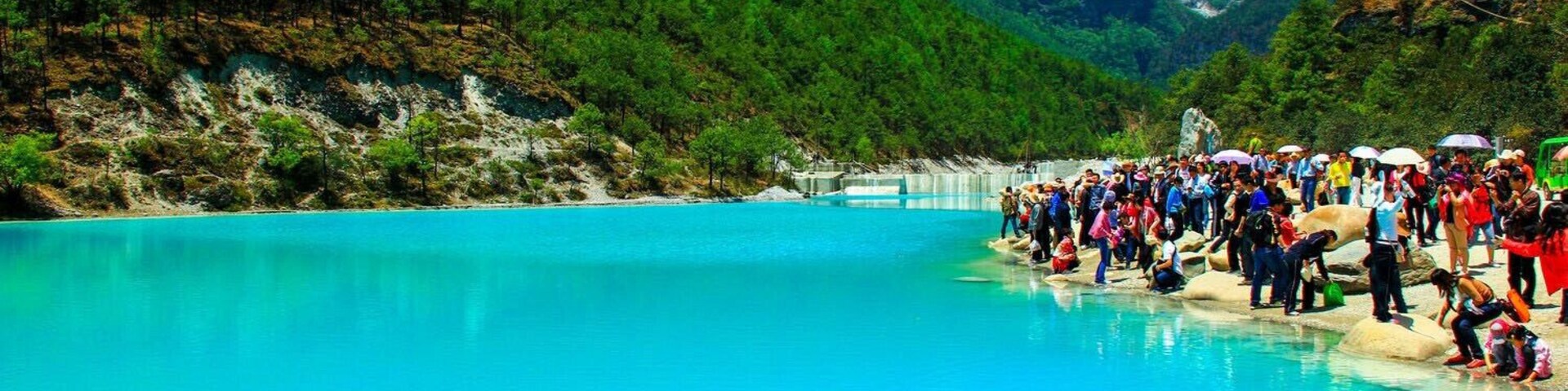 Un lago turquesa rodeado de montañas verdes y una multitud de personas.