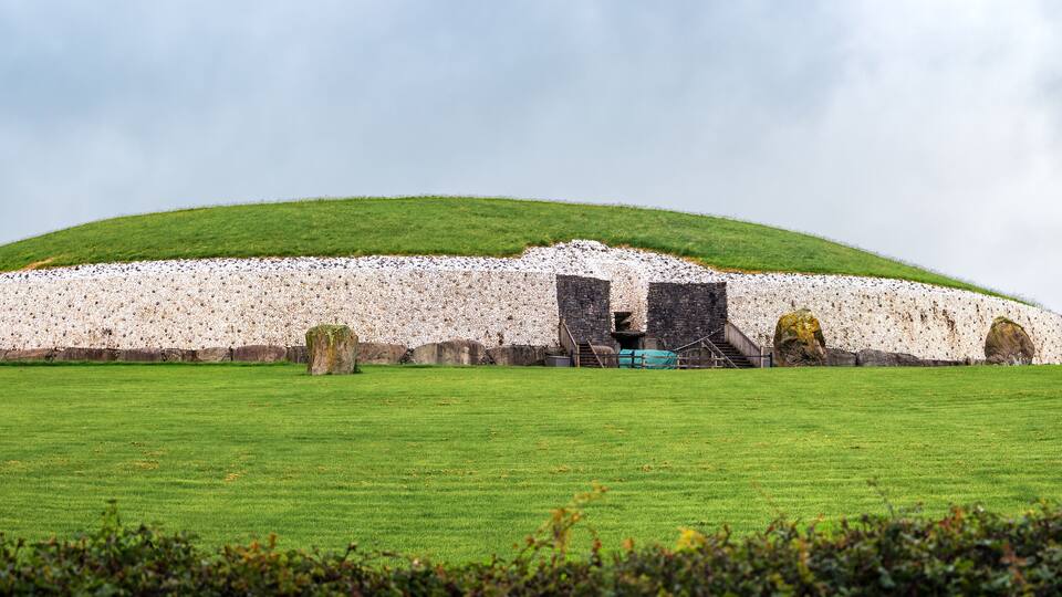 A large stone structure with a green roof, surrounded by a grassy field and several standing stones.