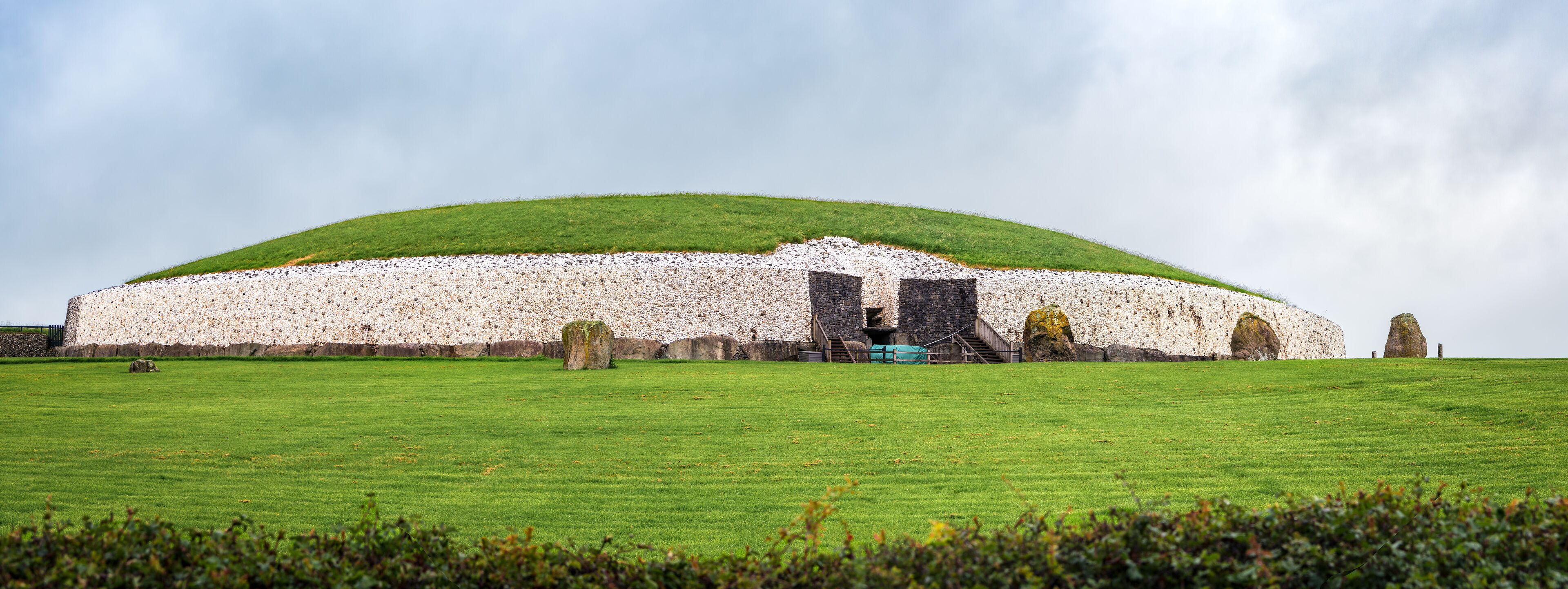 A large stone structure with a green roof, surrounded by a grassy field and several standing stones.
