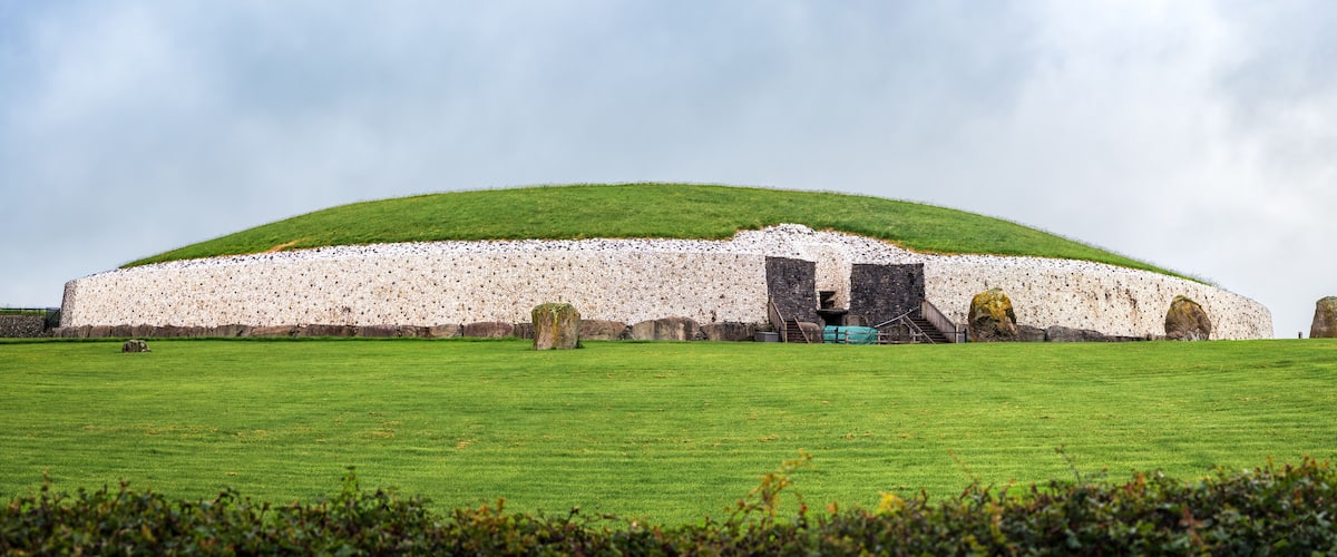 A large stone structure with a green roof, surrounded by a grassy field and several standing stones.