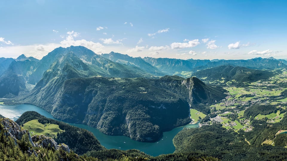 A mountainous landscape with a river, green valleys, and a clear sky.