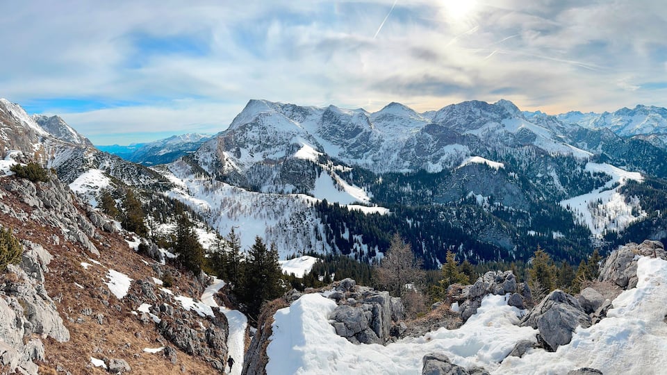 A snow-covered mountain range with a lake and a person hiking.