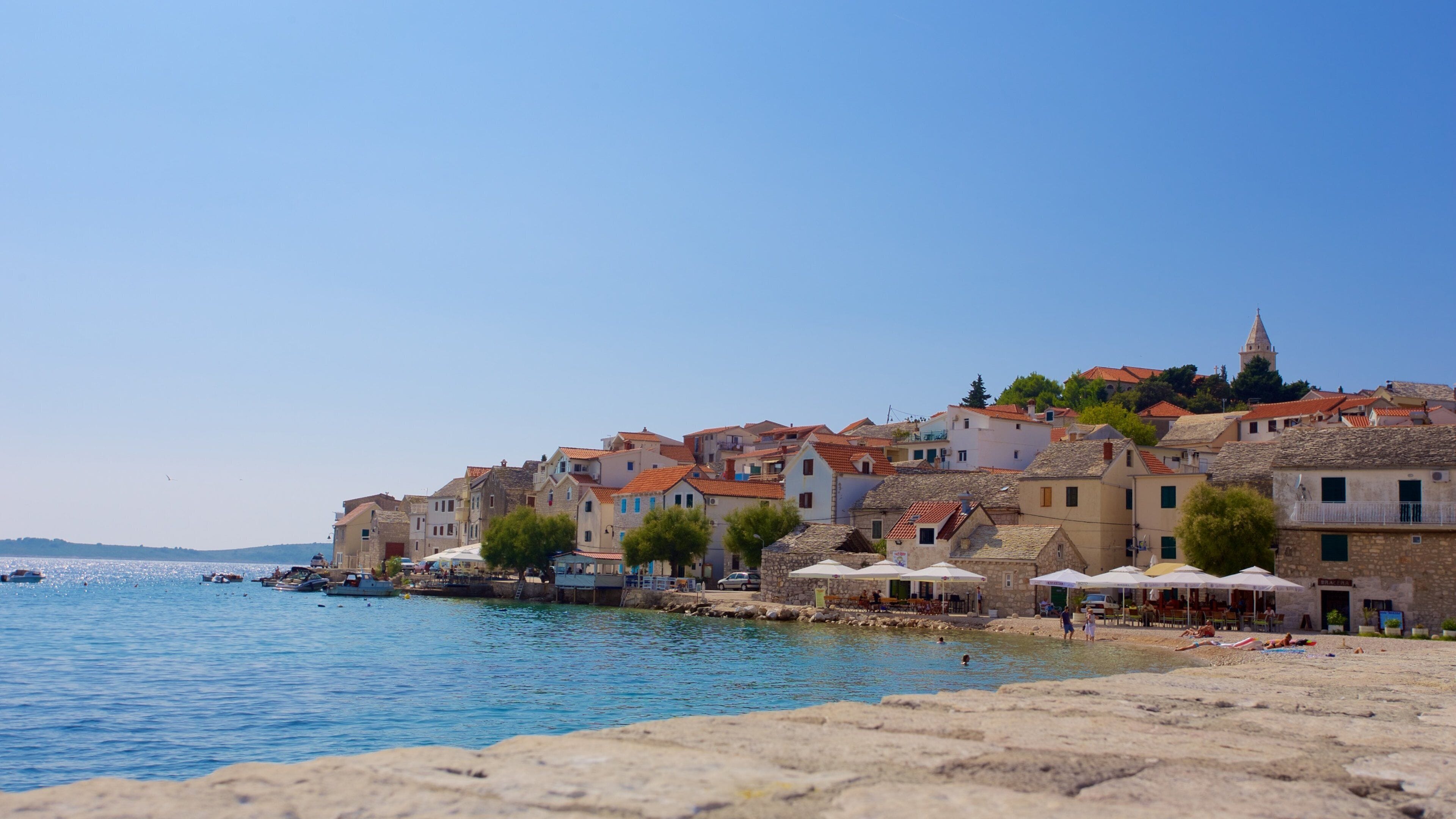 A coastal town with stone buildings, a clear blue sky, and boats on the water.