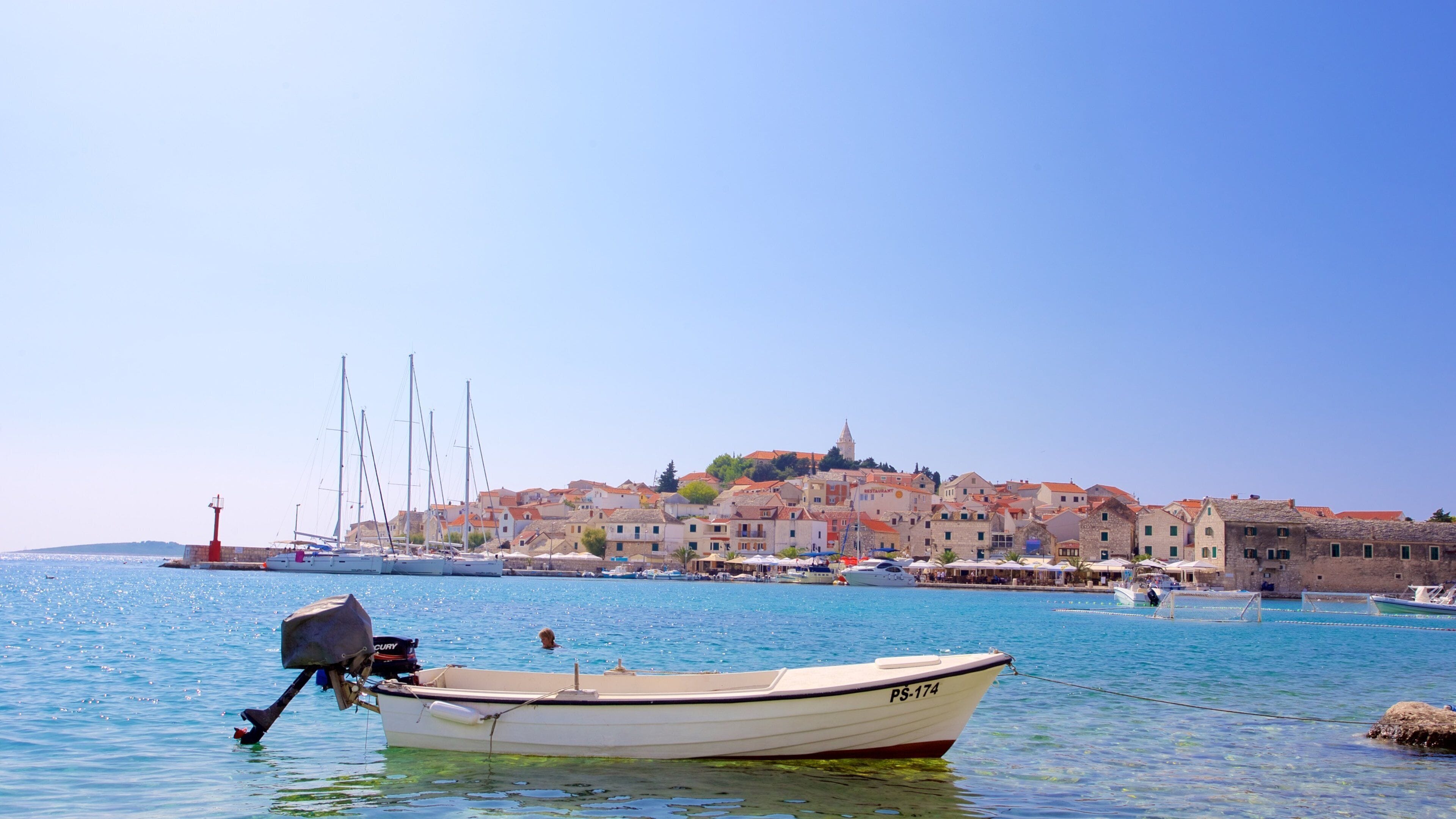 A coastal town with a historic church on a hill, boats docked along the waterfront, and a clear blue sky.