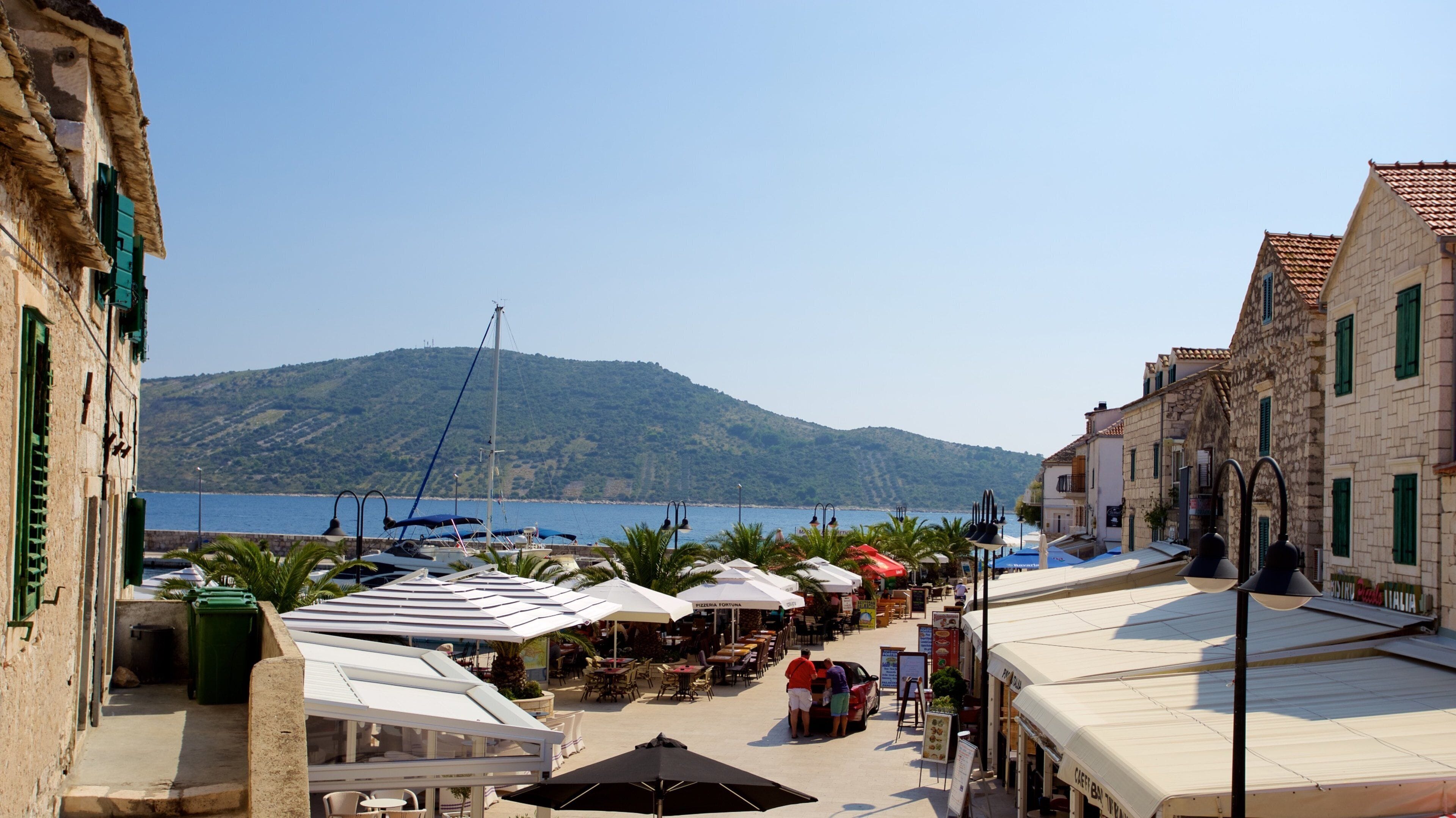 A coastal town with outdoor cafes, a marina, and a mountain in the background.