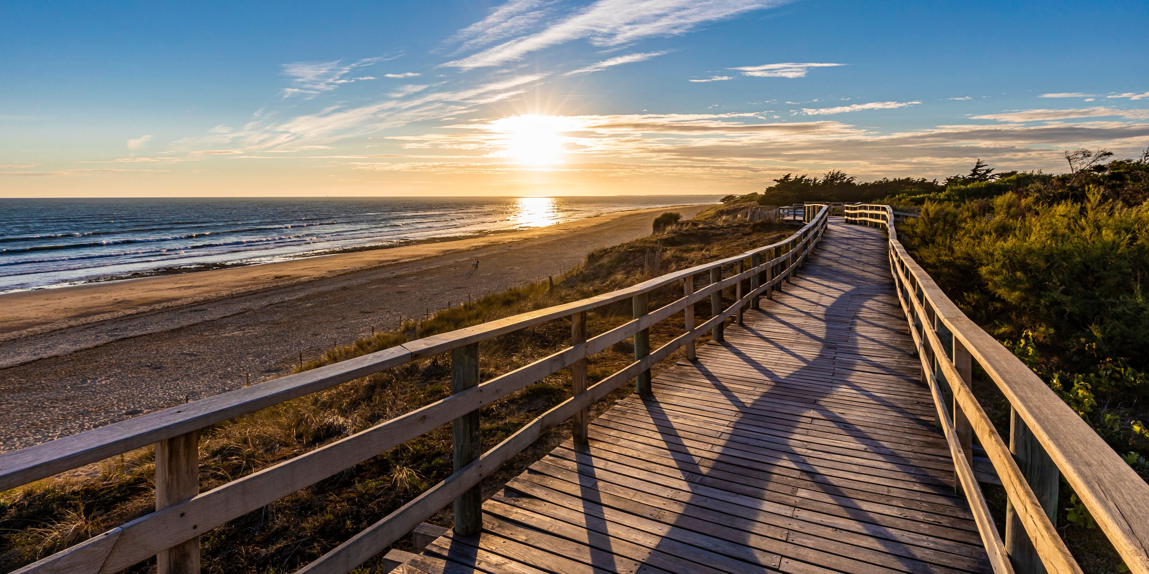 France, Nouvelle-Aquitaine, Le Bois-Plage-en-Re, Panoramic view of empty beachside boardwalk at sunset