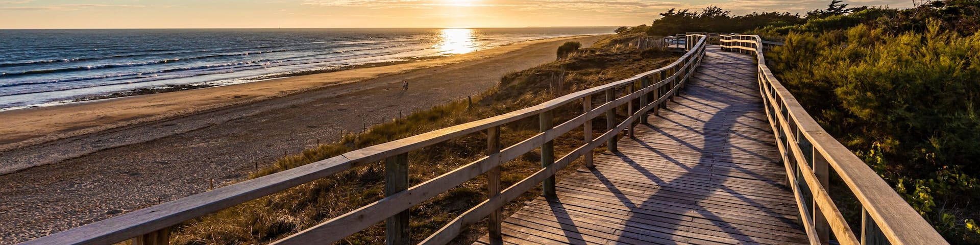 France, Nouvelle-Aquitaine, Le Bois-Plage-en-Re, Panoramic view of empty beachside boardwalk at sunset