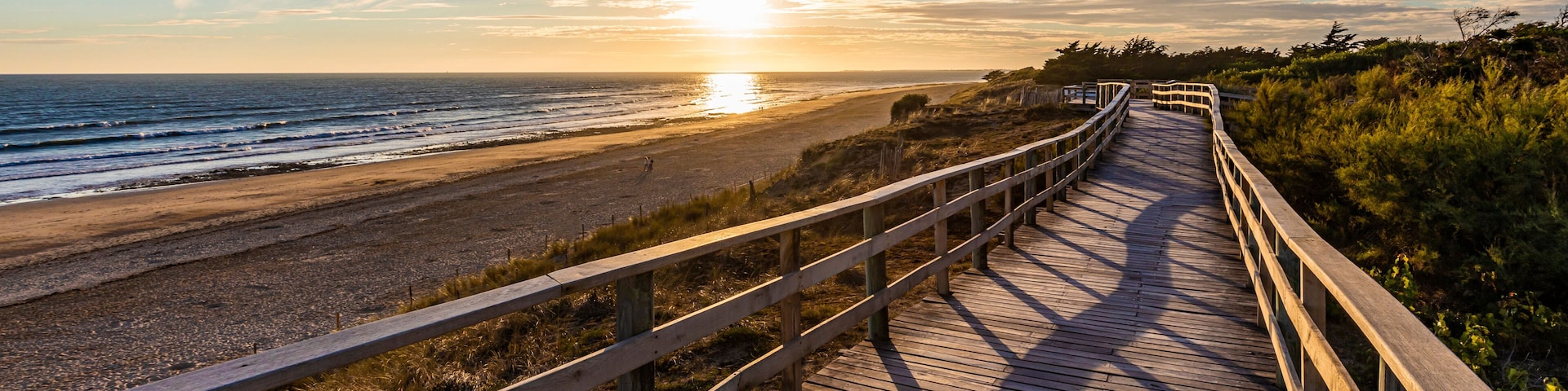 France, Nouvelle-Aquitaine, Le Bois-Plage-en-Re, Panoramic view of empty beachside boardwalk at sunset
