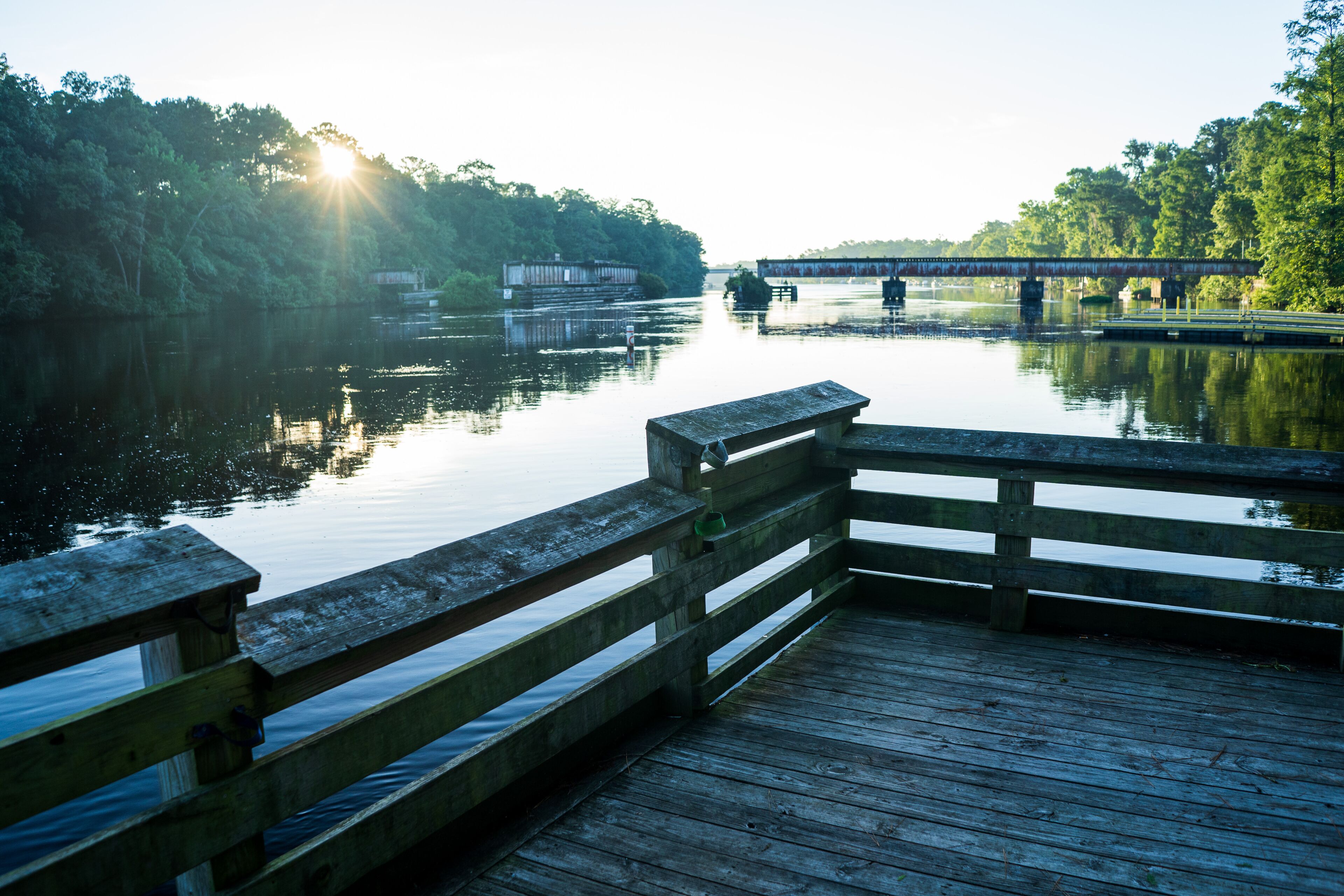 A wooden pier extending into calm water with a bridge in the background.