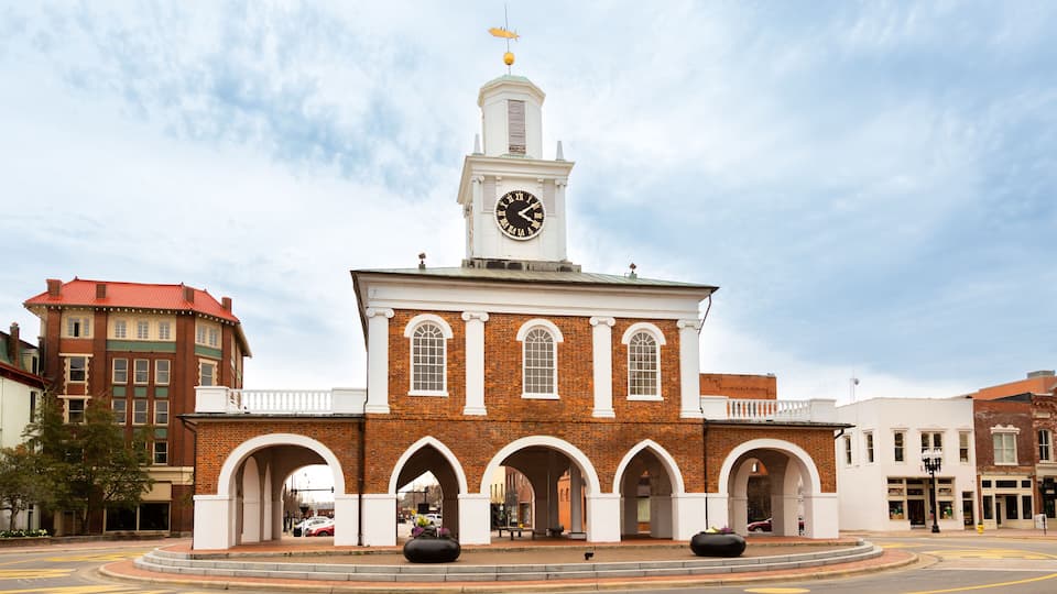 A historic clock tower with a white clock face, surrounded by brick buildings and a roundabout.