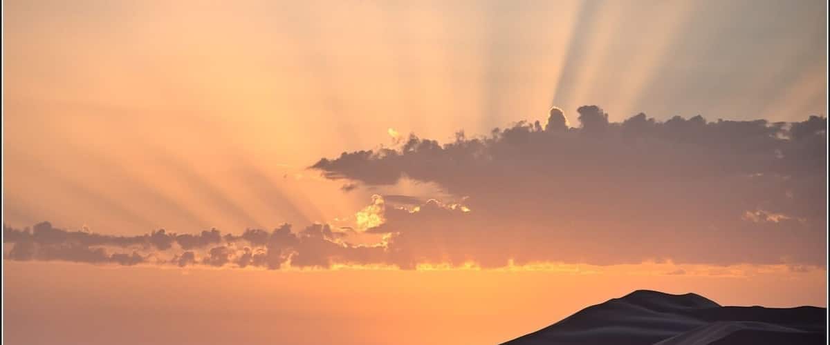 A desert landscape with sand dunes and a sunset.