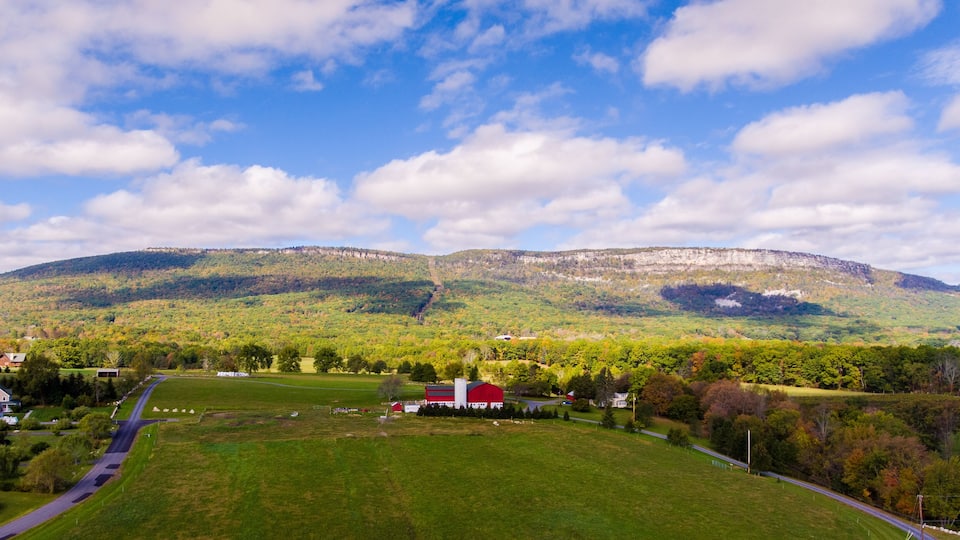 A green valley with a red barn, a road, and a mountain in the background.