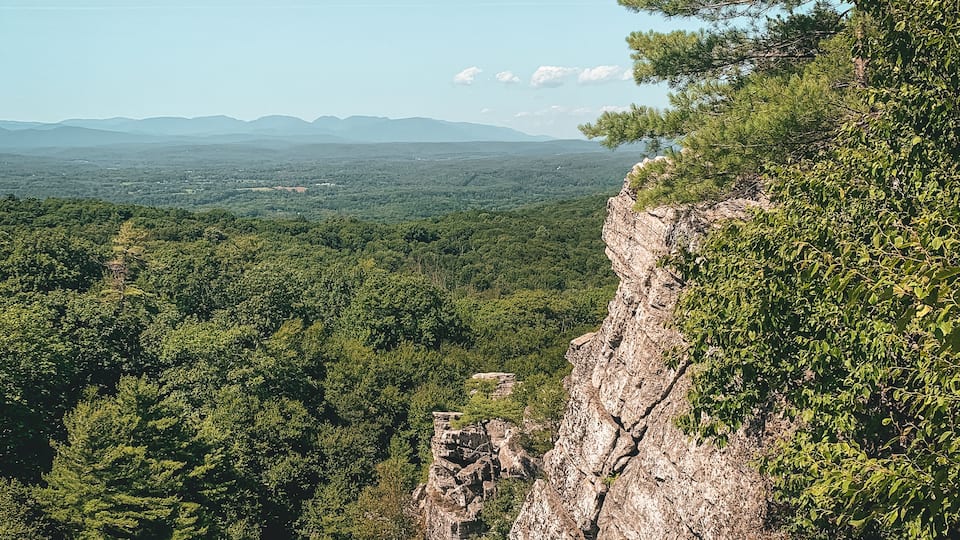 A mountainous landscape with dense forests, rocky cliffs, and a clear sky.