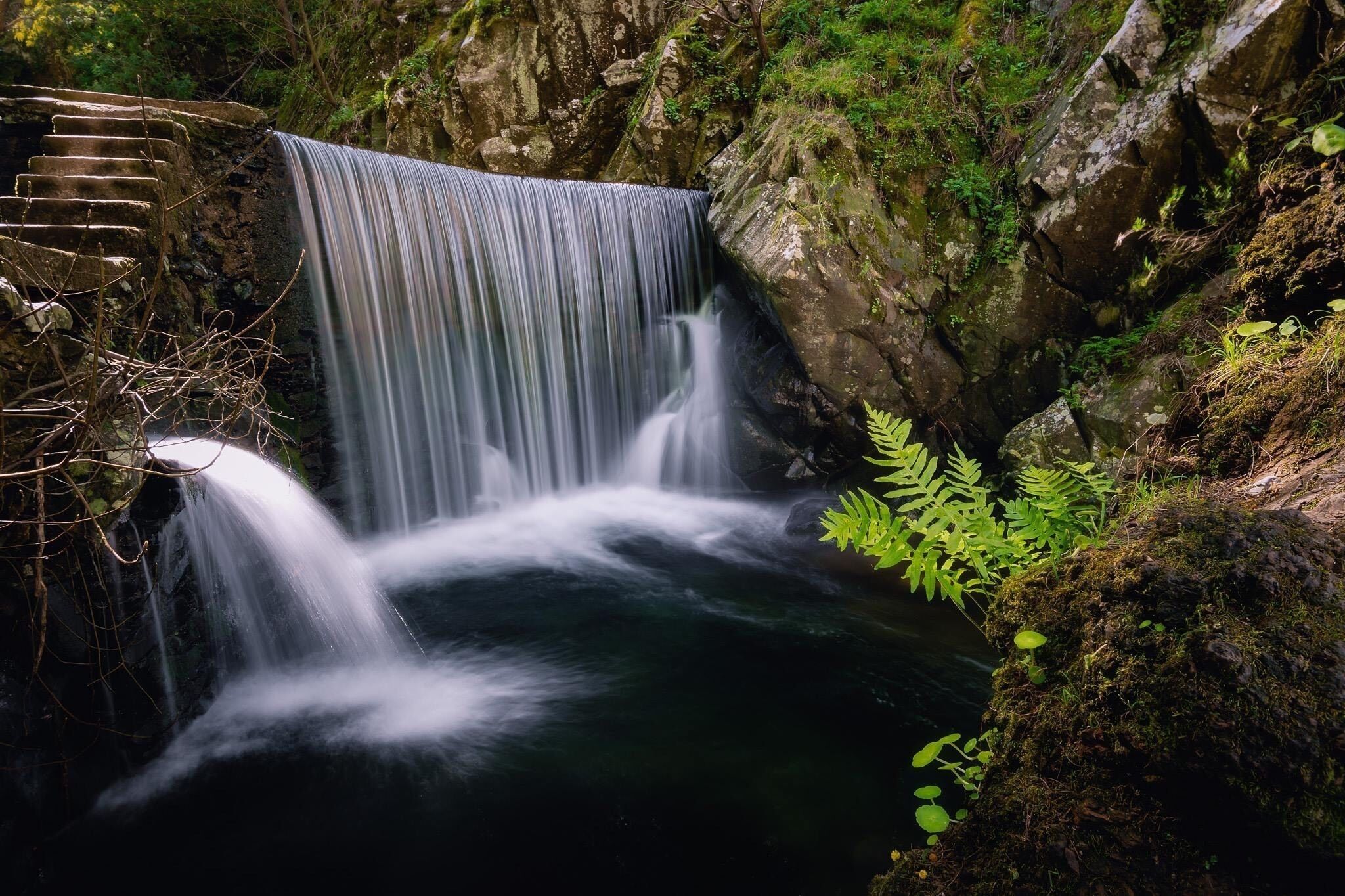 A waterfall cascading over moss-covered rocks in a forested area.
