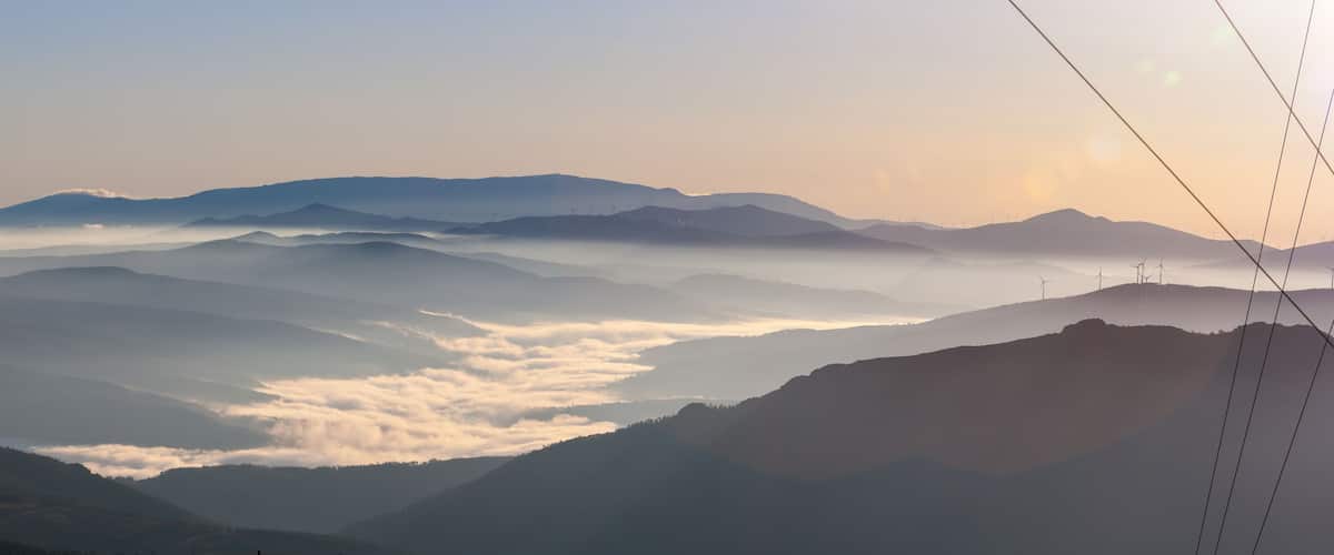 A mountainous landscape with rolling hills and wind turbines in the distance.