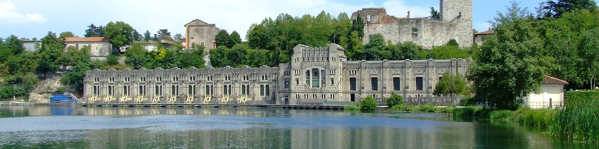 A historic building with a large tower, a castle, and a calm lake.