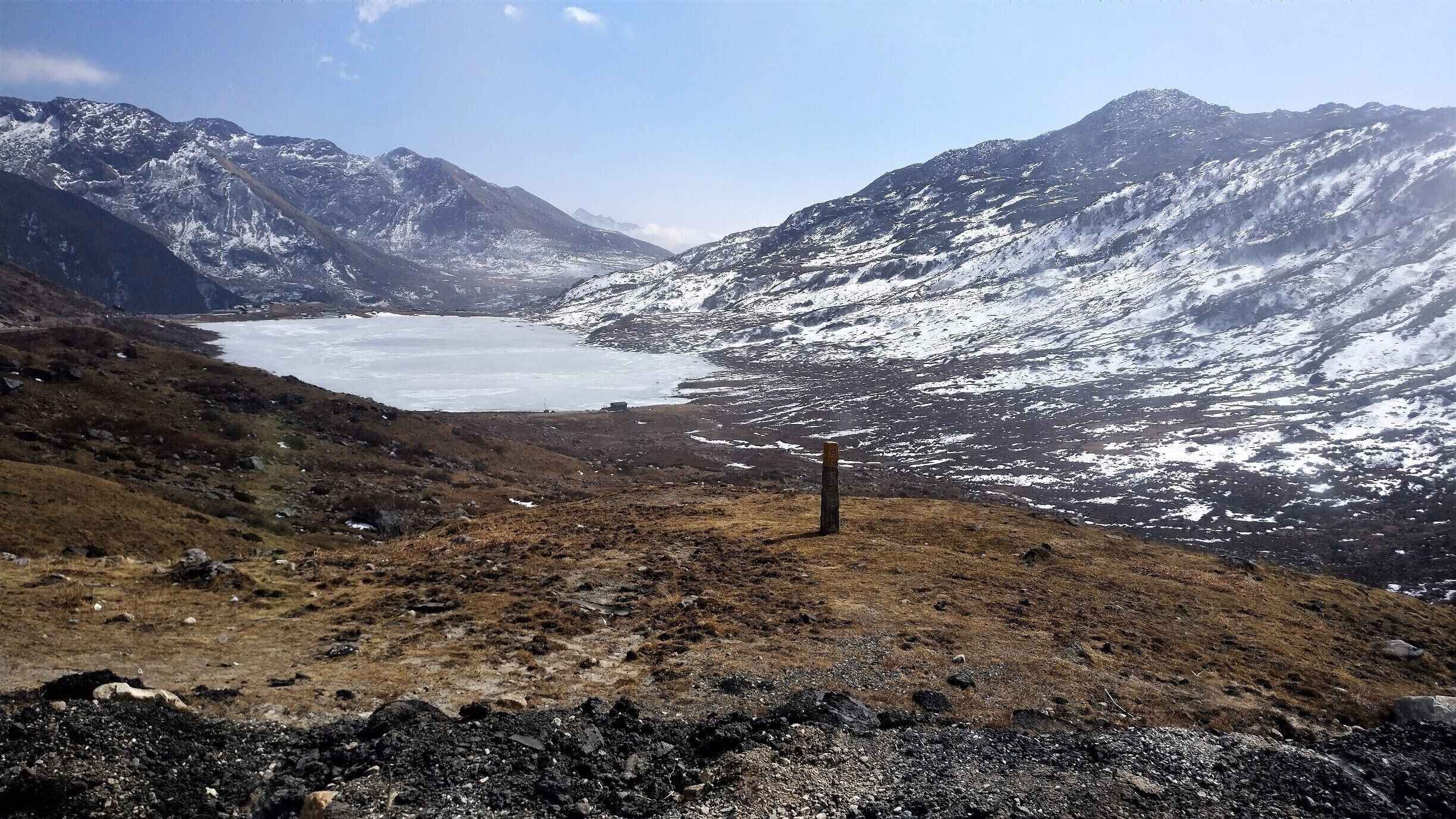 A mountainous landscape with a glacier and a wooden post in the foreground.
