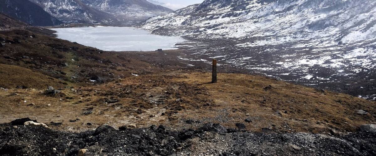 A mountainous landscape with a glacier and a wooden post in the foreground.