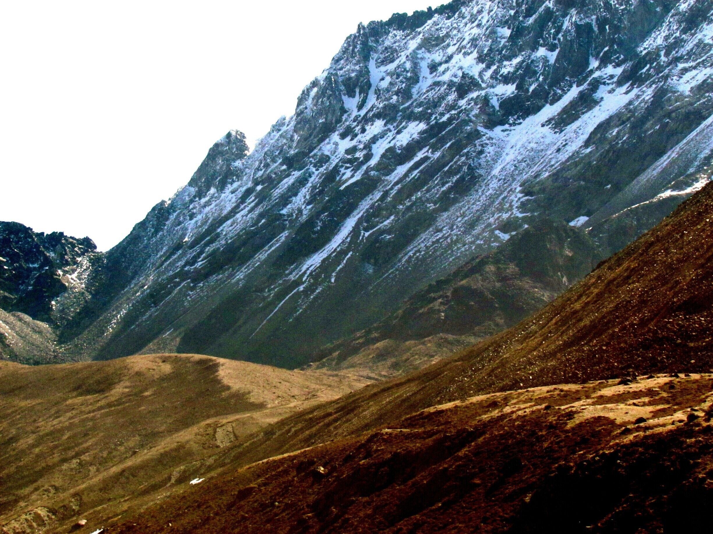 A rugged mountain landscape with snow-capped peaks and a valley.