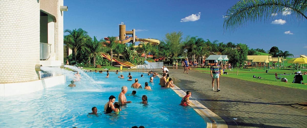 A swimming pool with people, a water slide, palm trees, and a water tower.