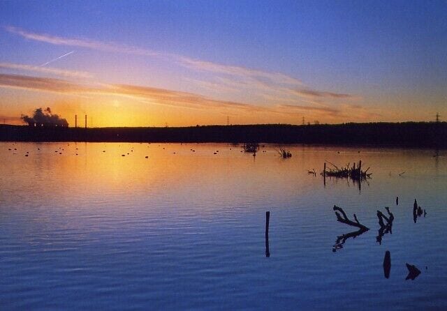 Un lago calmo al tramonto, con le sagome di alberi e imbarcazioni.