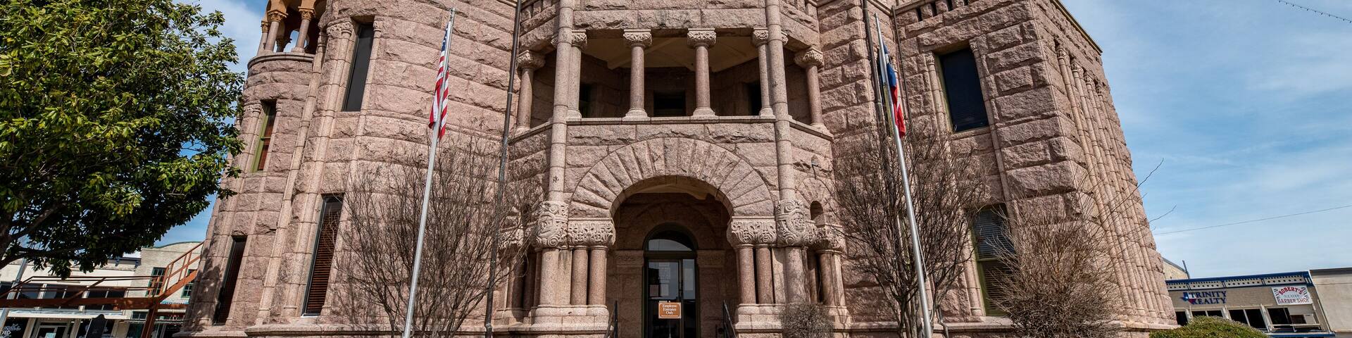 A historic stone building with a clock tower, arched entrance, and flagpoles.
