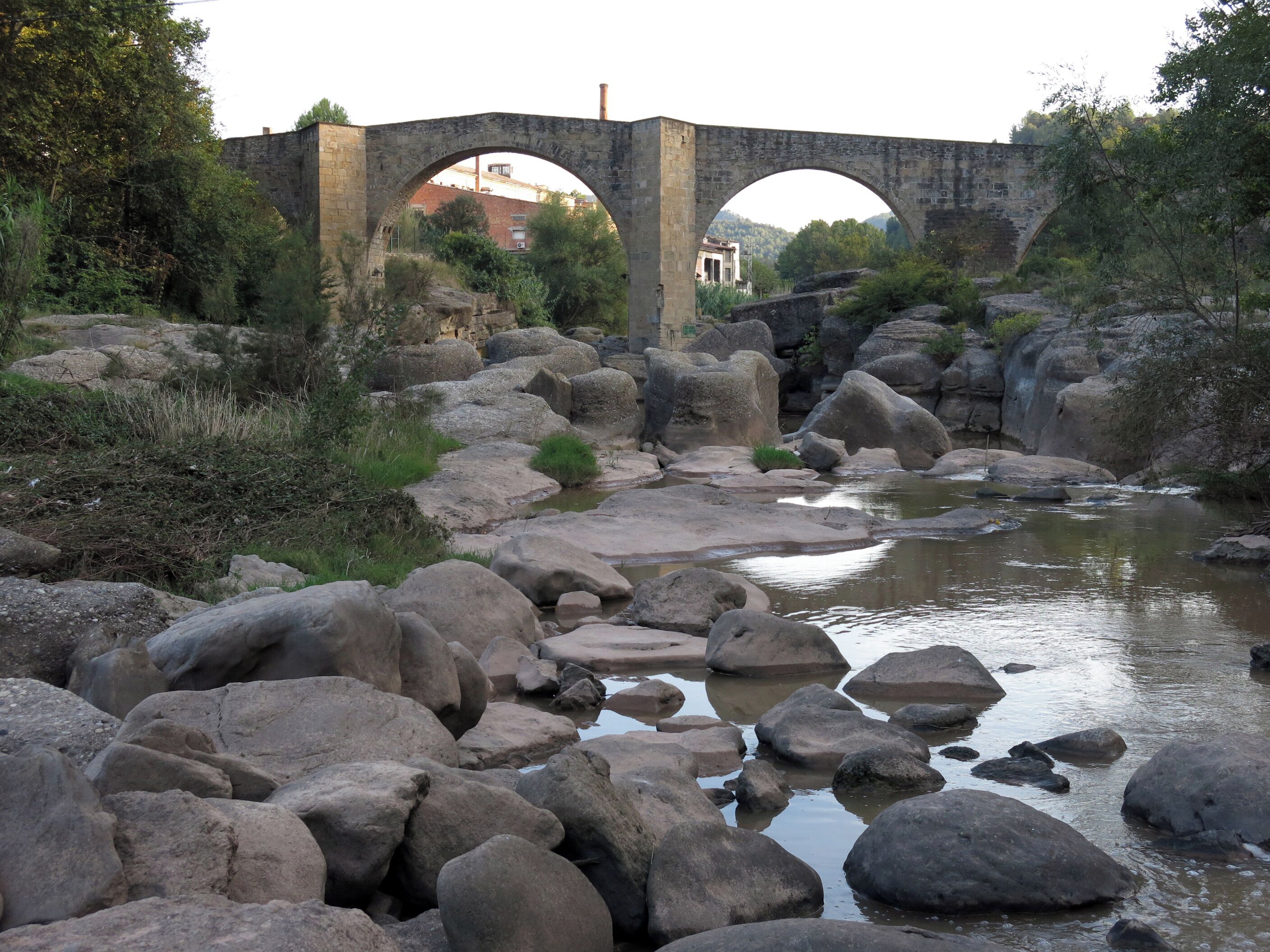 A stone bridge over a rocky stream with large boulders and greenery around.