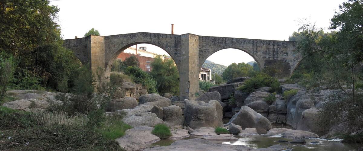 A stone bridge over a rocky stream with large boulders and greenery around.
